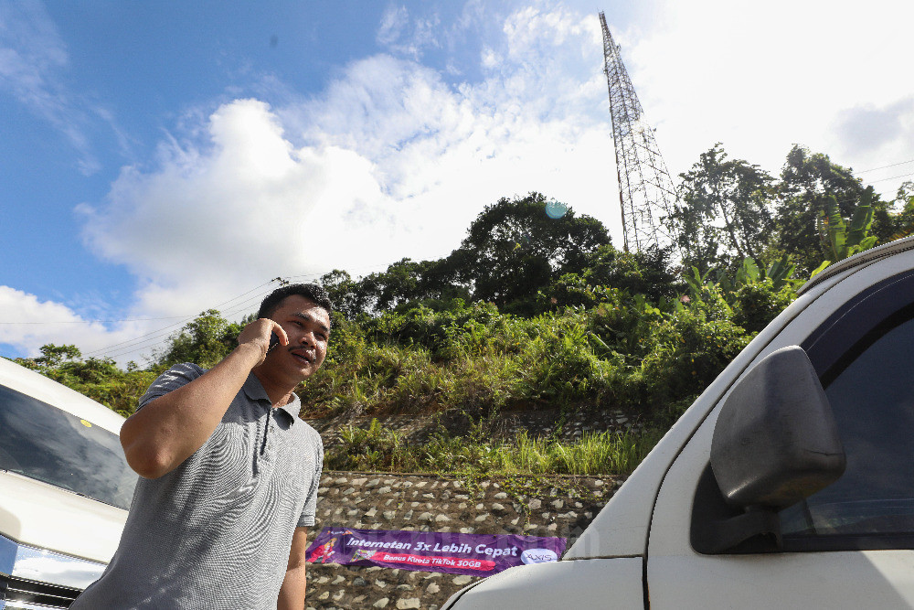 Warga menggunakan ponsel dengan latar BTS XL Axiata di Kecamatan Entikong, Kabupaten Sanggau, Kalimantan Barat, Kamis (9/2/2023). Dalam setahun terakhir, jumlah BTS XL Axiata bertambah sebanyak lebih dari 1.100 BTS 4G di seluruh wilayah Kalimantan, angka tersebut meningkat sebesar 42% YoY. Selain itu, infrastruktur jaringan XL Axiata di seluruh Kalimantan diperkuat oleh kabel fiber optic yang jalurnya telah membentang sepanjang lebih dari 9.300 kilometer. Bisnis/Eusebio Chrysnamurti