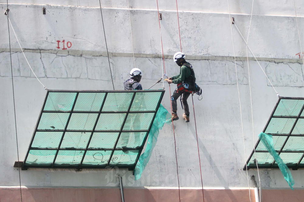 Pekerja bergelantungan mengerjakan perbaikan dinding salah satu pabrik di Makassar, Sulawesi Selatan, Rabu (31/5/2023). Kementerian Ketenagakerjaan (Kemenaker) mencatat sebanyak 13.634 pekerja mengalami pemutusan hubungan kerja atau PHK selama periode Januari-Maret 2023. Bisnis/Paulus Tandi Bone