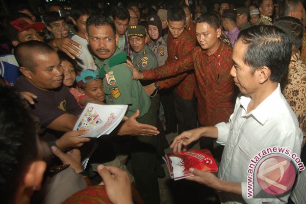 Presiden Joko Widodo (kanan) membagikan buku kepada ribuan warga, di Desa Seberang Pebayan, Padang, Sumatera Barat, Senin (4/7/2016) malam.