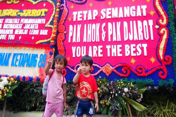 Dua anak berfoto di depan rangkaian bunga untuk Ahok dan Djarot di Balai Kota DKI Jakarta, Kamis (27/4/2017)./Bisnis.com-Miftahul Khoer