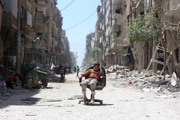 Seorang anak laki-laki duduk di kursi di sepanjang jalan yang rusak di kota Douma di Damaskus, Suriah pada 16 April 2018./Reuters