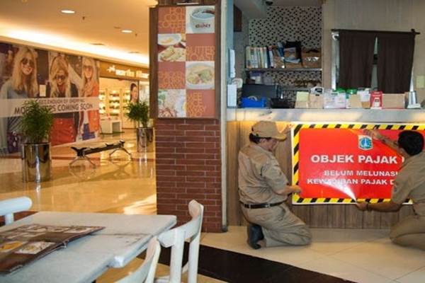 Petugas Pajak Jakarta Selatan memasang stiker pemberitahuan utang pajak di sebuah kedai di Pondok Indah Mall 2, Jakarta./Antara