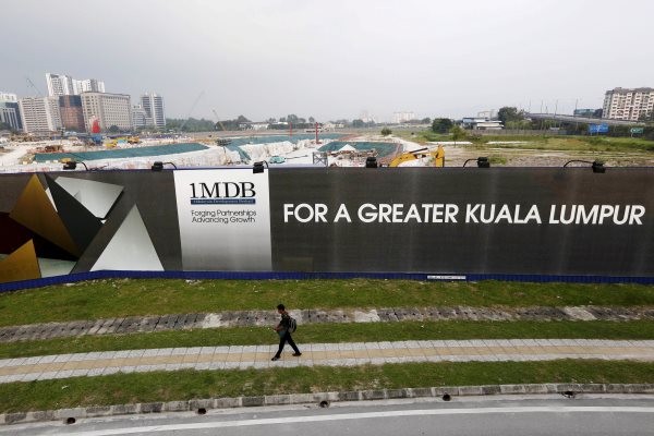 Seorang pejalan kali melintas di depan bilboard 1 Malaysia Development Berhad (1MDB) di  Kuala Lumpur (1/3/2015)./Reuters-Olivia Harris