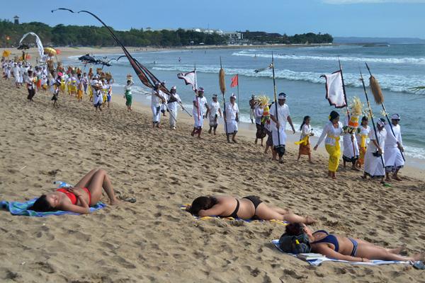 Wisatawan berjemur saat umat Hindu melaksanakan upacara Melasti di Pantai Kuta, Badung, Bali, Sabtu (25/3)./Antara-Fikri Yusuf