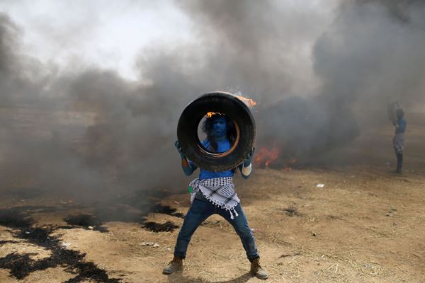 Seorang demonstran dengan wajah dicat seperti karakter dari film Avatar membawa ban terbakar selama protes oleh warga Palestina yang menuntut hak untuk kembali ke Tanah air mereka, di perbatasan Israel-Gaza di Jalur Gaza selatan./Reuters