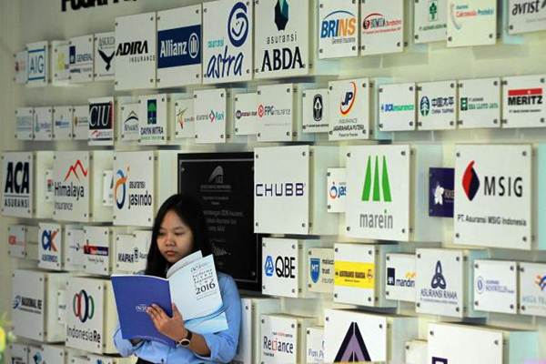 Karyawati berdiri di dekat logo beberapa perusahaan asuransi di kantor Asosiasi Asuransi Umum Indonesia di Jakarta, Senin (8/1)./JIBI-Dwi Prasetya