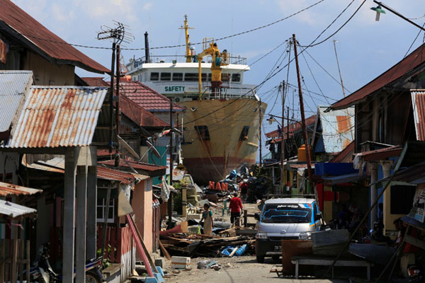 Warga berjalan di depan rumah mereka yang dihantam gempa dan tsunami di Desa Wani, Donggala, Sulawesi Tengah, di dekat kapal feri KM Sabuk Nusantara 39 yang terangkat dari lautan ke daratan. Gempa dan tsunami terjadi pada Jumat (28/9/2018) menjelang malam, foto diambil pada Selasa (2/10/2018)./Reuters-Beawiharta