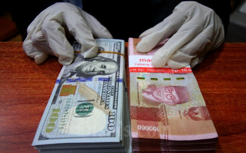 Petugas menunjukkan uang rupiah dan dolar AS di salah satu gerai penukaran mata uang asing di Jakarta, Kamis (19/3/2020)./Bisnis-Arief Hermawan P