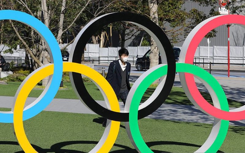 Seorang pejalan kaki sambil mengenakan masker melintas di dekat logo olimpiade di kota Tokyo, Jepang (12/3/2020)/Antara.