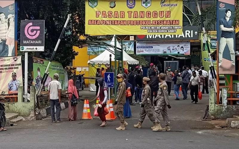 Petugas Satpol PP melintas di depan pintu masuk Pasar Perumnas Klender, Jakarta Timur, pada hari pertama penerapan mekanisme ganjil genap kios pedagang, Senin (15/6/2020)./Antara