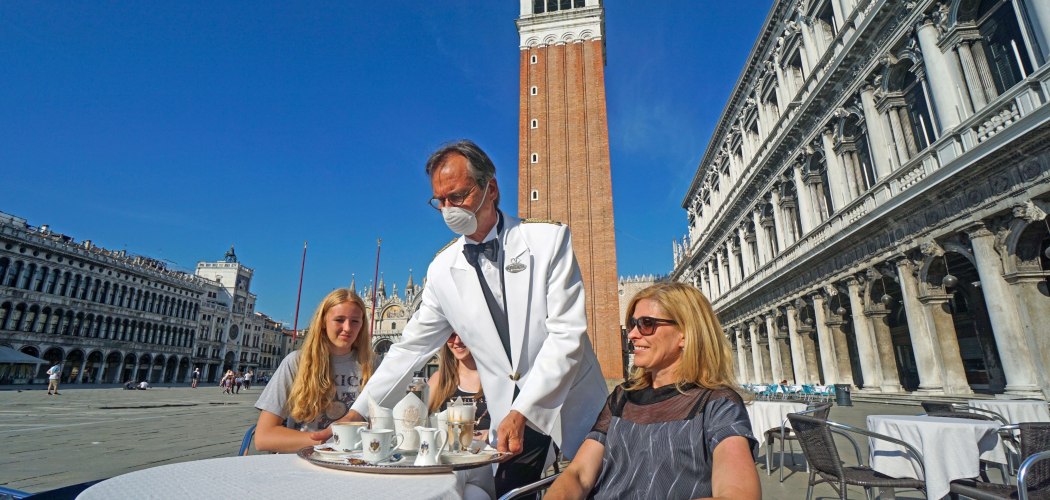 Seorang pelayan mengenakan masker melayani pelanggan di Cafe Florian di Piazza San Marco di Venesia, Italia, Jumat (12/6/2020). - Bloomberg/Andrea Merola