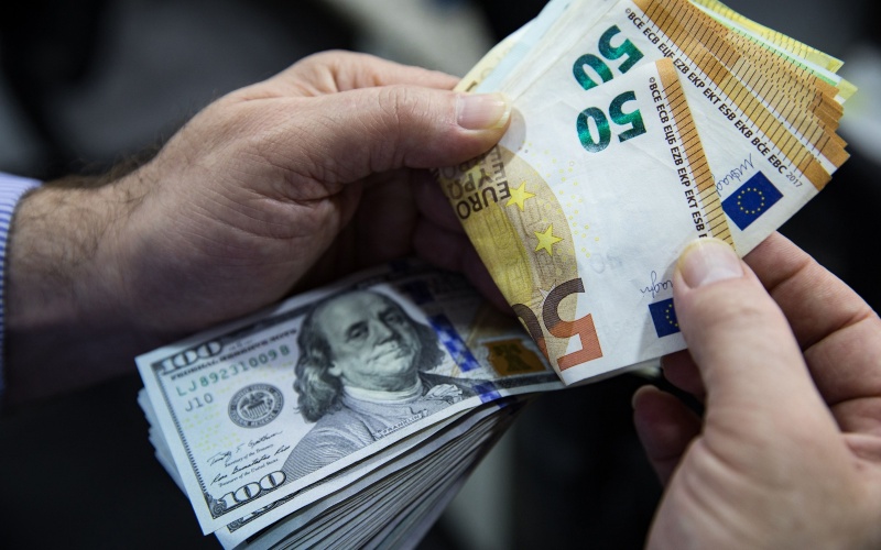 Seorang pria menghitung lembaran uang euro dan dolar AS./Bloomberg-Kerem Uzel