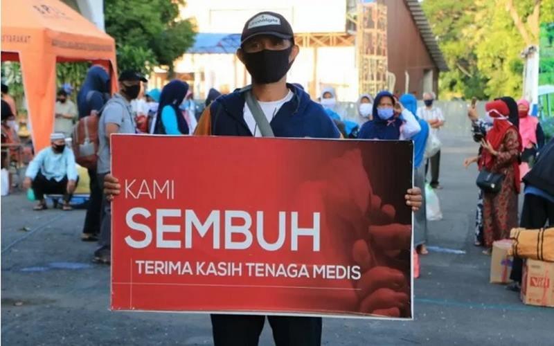 Seorang warga yang dinyatakan sembuh dari Covid-19 membawa spanduk bertuliskan ucapan terima kasih kepada tenaga medis saat dipulangkan dari tempat karantina di Asrama Haji Surabaya pekan lalu./Antara