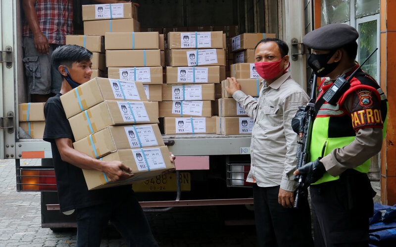 Polisi mengawasi pekerja yang mengangkut karton berisi surat suara di Komisi Pemilihan Umum (KPU) Kabupaten Gresik, Jawa Timur, Minggu (22/11/2020)./Antara-Didik Suhartono