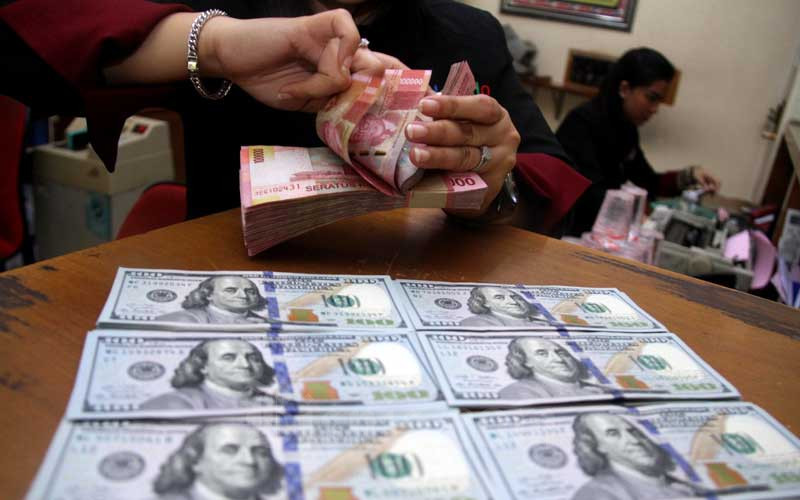 Petugas menunjukkan uang rupiah dan dolar AS di salah satu gerai penukaran mata uang asing di Jakarta, Senin (16/3/2020). Bisnis/Arief Hermawan P 