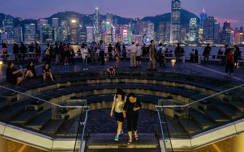 Warga Hong Kong menikmati malam di tepi laut di distrik Tsim Sha Tsui sambi menyaksikan properti di seberang Pelabuhan Victoria terang benderang,/Bloomberg/Anthony Kwan