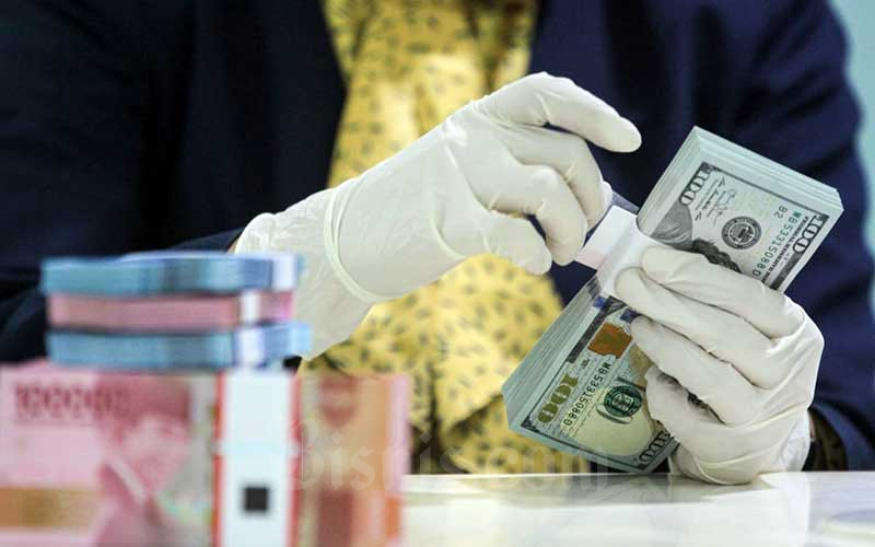 Karyawati salah satu bank memperlihatkan uang rupiah dan dolar di Jakarta, Kamis (29/4/2021). Bisnis/Arief Hermawan P