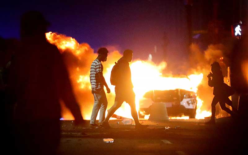 Demonstran berjalan di depan sebuah mobil polisi yang telah terbakar saat protes  atas kematian George Floyd di Boston, Amerika Serikat, Minggu (31/5/2020). Bloomberg/Getty Images/Maddie Meyer