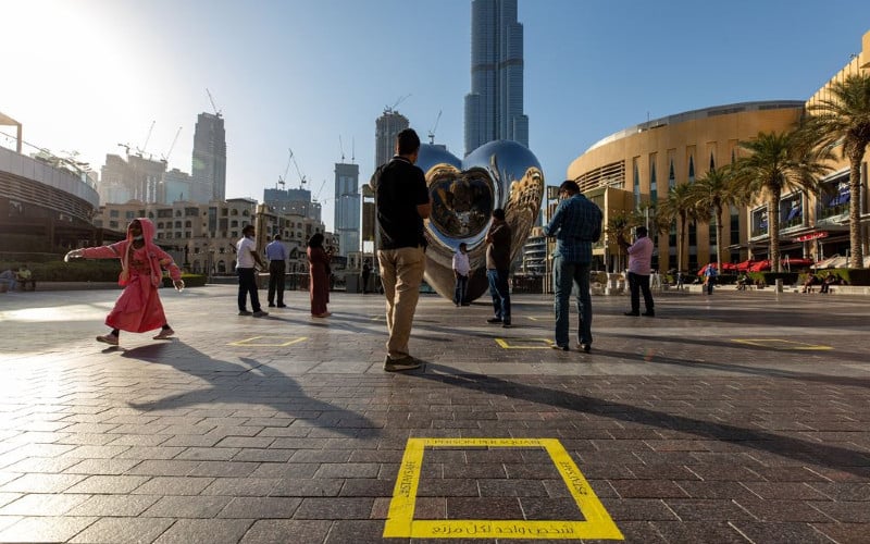 Turis berdiri di antara tanda-tanda lantai jarak sosial di dekat gedung pencakar langit Burj Khalifa di Dubai. /Bloomberg-Christopher Pike 