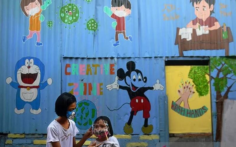 Dua orang anak menggunakan masker pelindung wajah saat bermain di depan mural bertema Covid-19 di Jakarta, Senin (27/7/2020)./Antarann