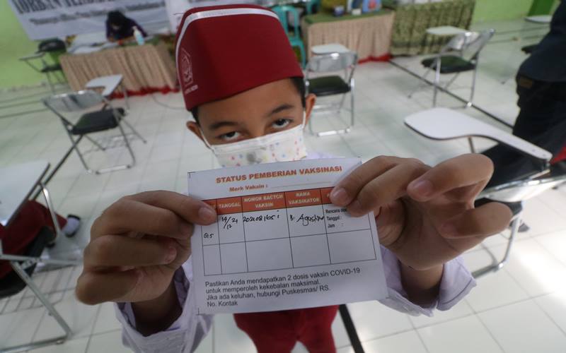 Seorang anak memperlihatkan kartu vaksinasi usai mendapatkan suntikan vaksin COVID-19 di Madrasah Ibtidaiyah Negeri 2 Kediri, Jawa Timur, Selasa (14/12/2021). Pemerintah akan menggunakan 6,4 juta dosis vaksin Sinovac untuk anak hingga akhir Desember 2021. ANTARA FOTO/Prasetia Fauzani/