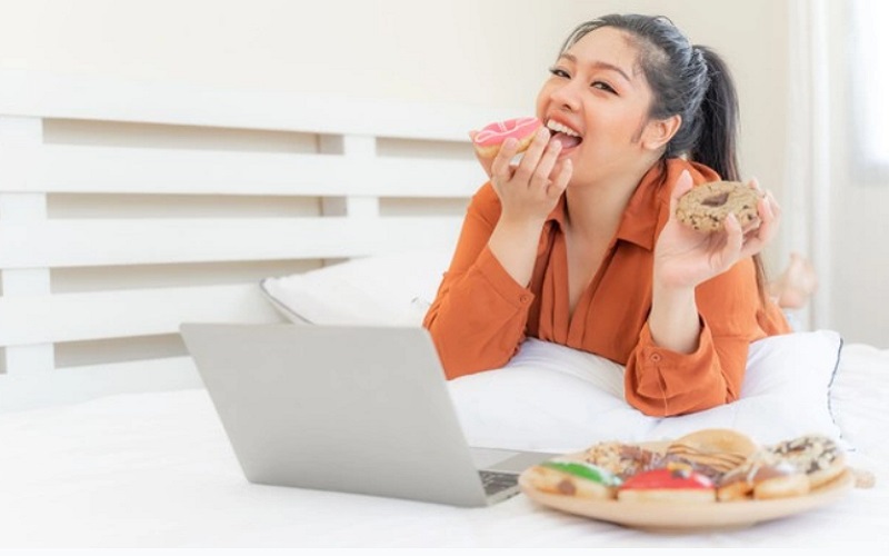 Ilustrasi perempuan makan sambil nonton yang bisa membuat berat badan naik/Freepik