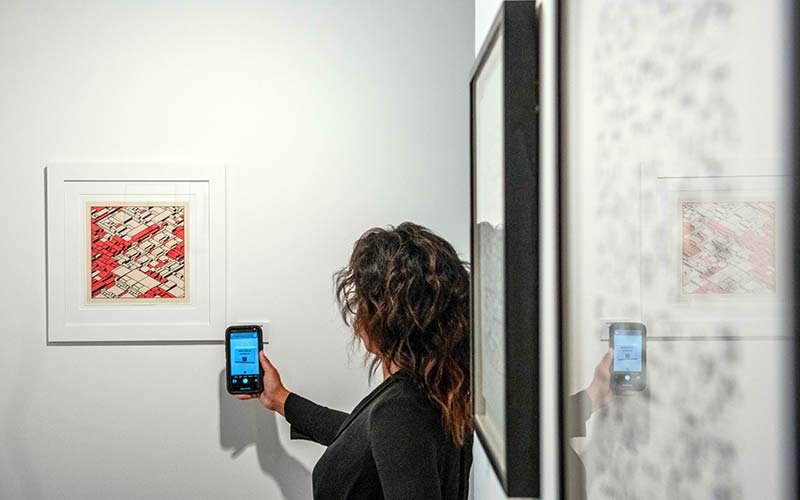 Pengunjung memegang smartphone yang menampilkan pasar online galeri di dekat NFT dan tandatangan litograf di  Gallery di London, Inggris, Rabu (22/9/2021). Bloomberg/Chris J. Ratcliffe