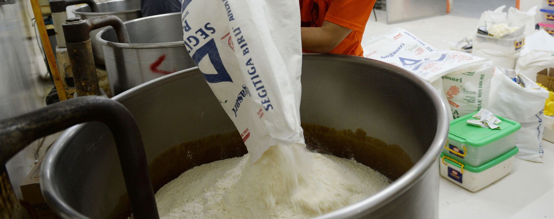 Seorang karyawan menuangkan sekantong tepung terigu ke dalam mesin pencampur untuk menyiapkan adonan di pabrik roti Tan Ek Tjoan di Ciputat, Provinsi Banten, Indonesia. /Bloomberg