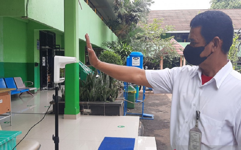Salah satu tenaga kependidikan sedang memeriksa suhu tubuh sebelum memasuki ruangan sekolah pada saat PTM terbatas di SMA N 46 Jakarta, Rabu (15/9/2021). ANTARA/Sihol Hasugian