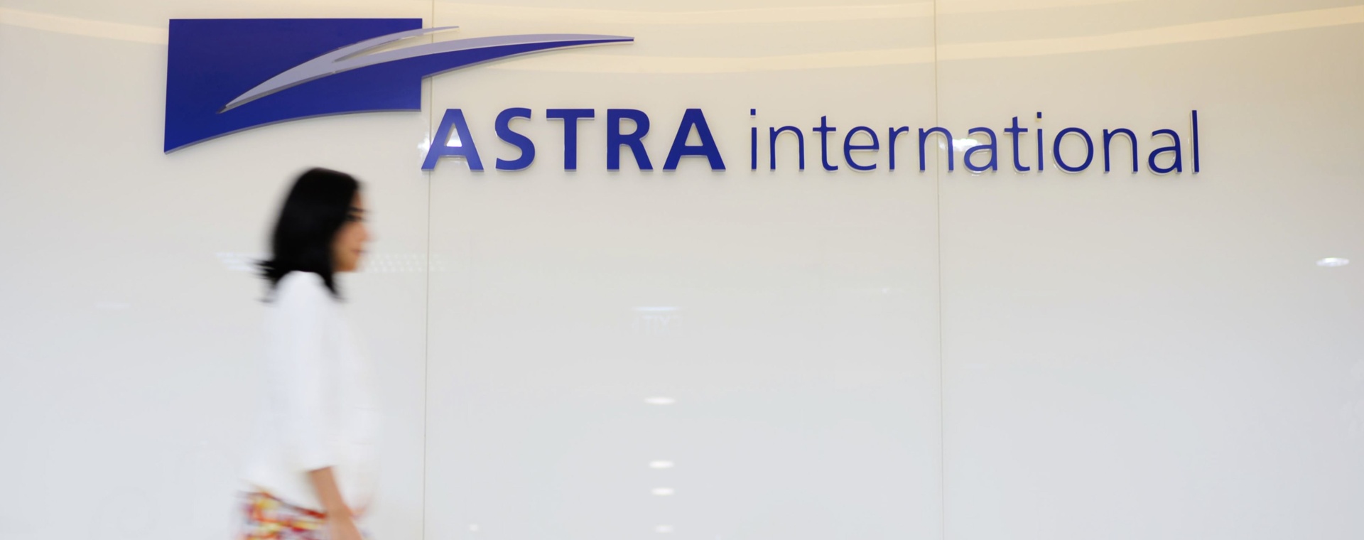 Seorang wanita berjalan melewati papan nama PT Astra International Tbk. (ASII), di Jakarta, Rabu (4/6/2014). Bloomberg - Dimas Ardian