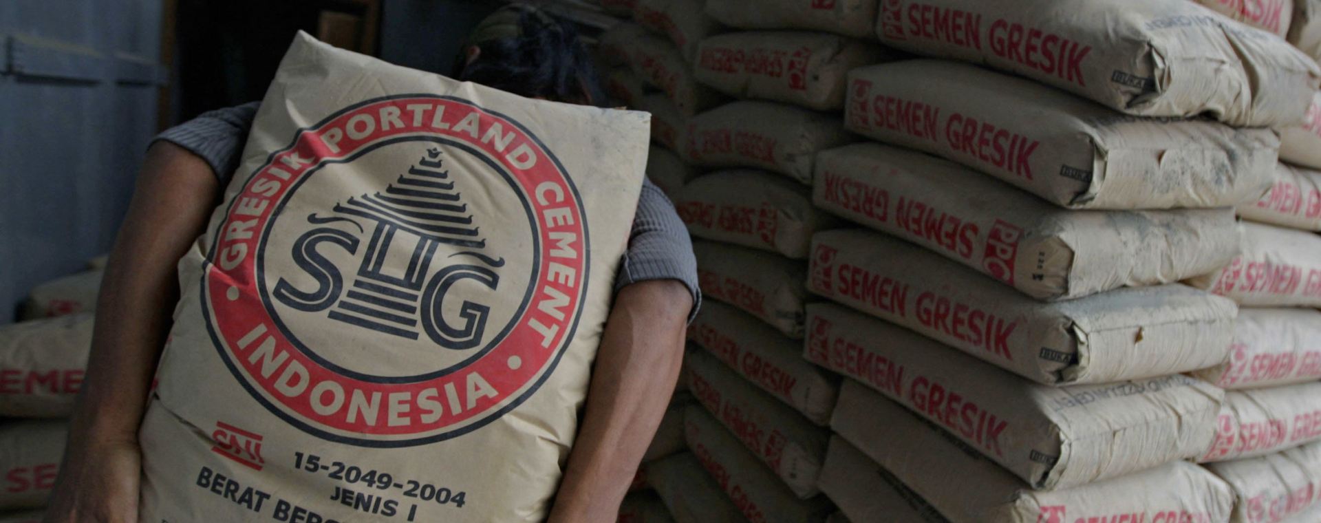 Seorang pekerja membawa kantong semen Semen Gresik di sebuah toko di Jakarta, Senin, (5/11/2007). Bloomberg - Dimas Ardian