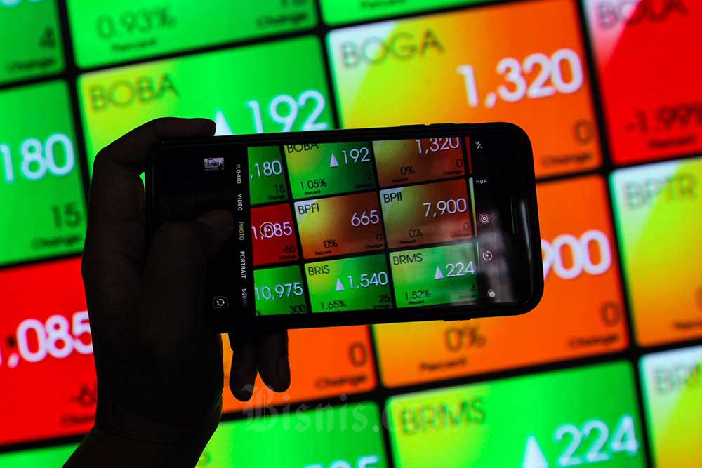 Karyawan menggunakan ponsel di dekat layar pergerakan indeks harga saham gabungan (IHSG) di Bursa Efek Indonesia, Jakarta, Rabu (20/7/2022). Bisnis/Fanny Kusumawardhani