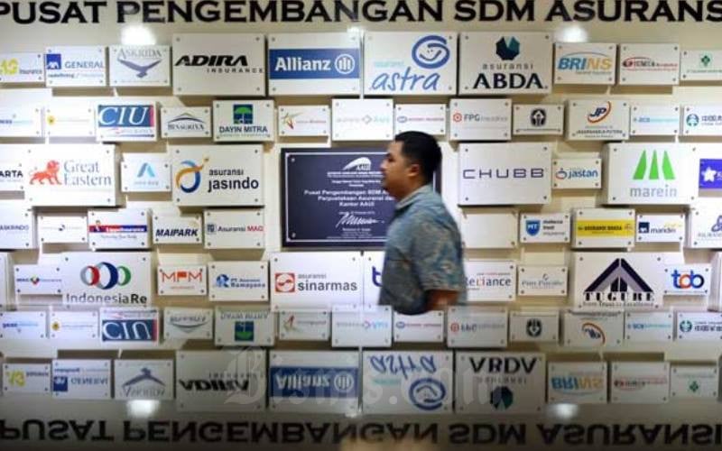 Karyawan melintasi logo-logo perusahaan asuransi di Kantor Asosiasi Asuransi Umum Indonesia (AAUI), Jakarta, Selasa (11/02/2020). Bisnis/Eusebio Chrysnamurti