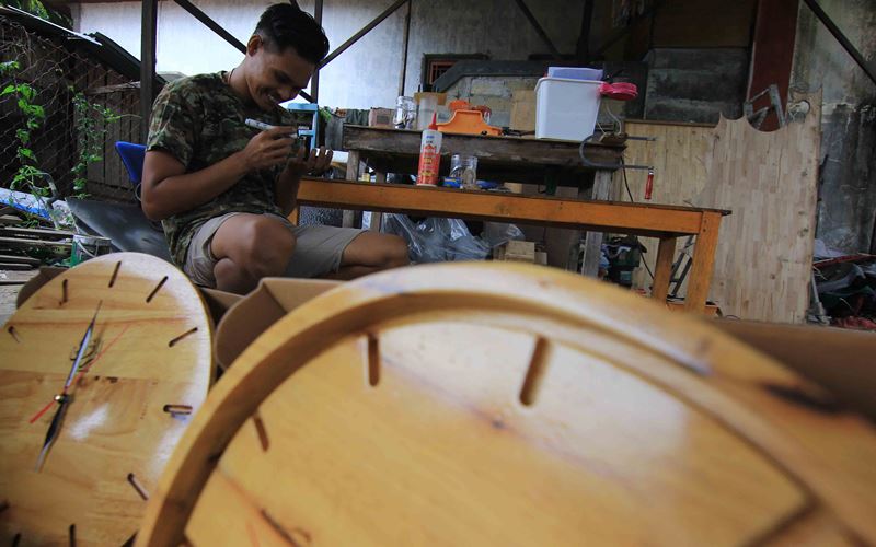 Doni tengah membuat jam dinding estetik kayu di rumah produksi di daerah Limau Manis, Kecamatan Pauh, Kota Padang, Sumatra Barat, Senin (21/11/2022). Usaha Ekonomi Produktif Ar-Razzaq Jam Dinding Estetik ini lahir dari tiga orang lulusan SMK di Padang. Karya jam dinding estetik kayu yang diproduksi itu dipelajari melalui video yang tersebar di media sosial. Harga jual jam dinding estetik kayu tersebut mulai dari Rp80.000 hingga Rp300.000 per unitnya. Bisnis/Muhammad Noli Hendra