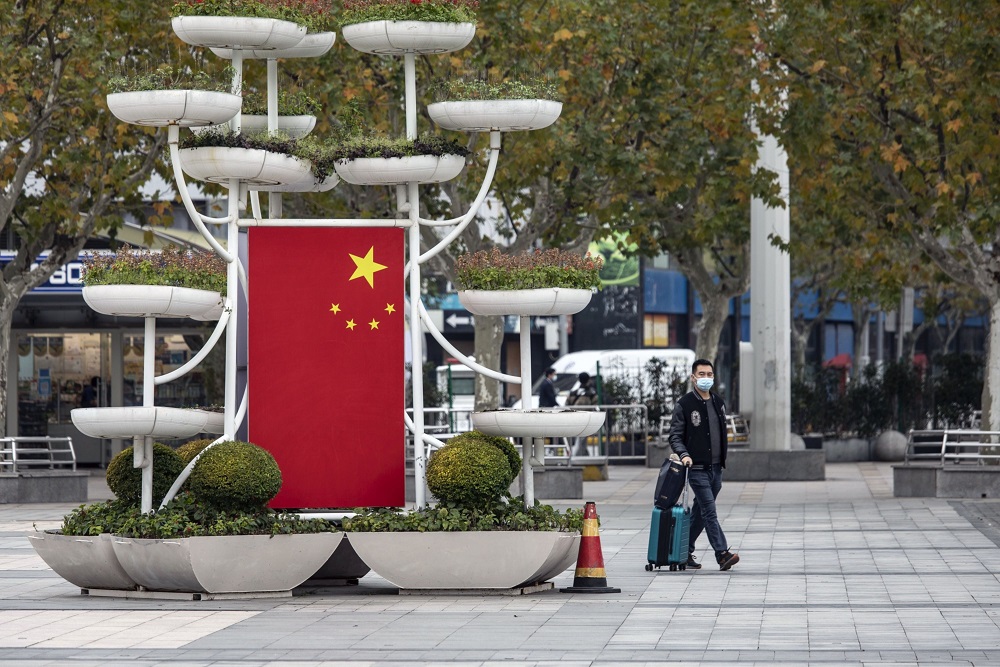Salah satu warga negara China berjalan di taman dengan tetap memakai masker seiring meningkatkan kasus Covid-19 di negara tersebut. / Bloomberg. 