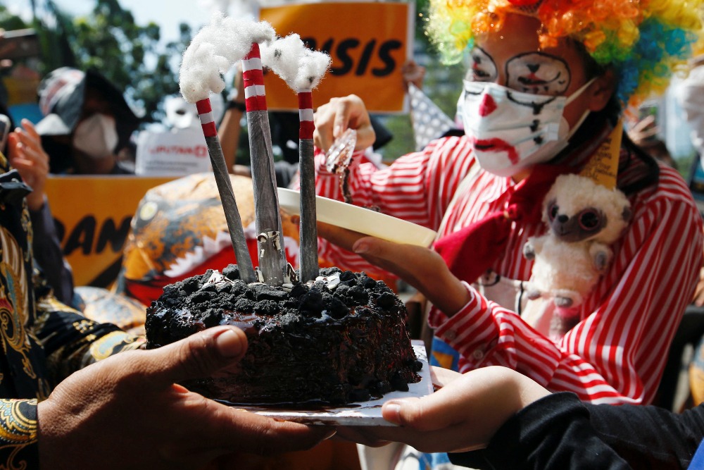 Seorang aktivis mengenakan kostum badut memotong kue ulang tahun yang menggambarkan asap dan uap mengepul dari pembangkit listrik tenaga batu bara. - REUTERS - Ajeng Dinar Ulfiana