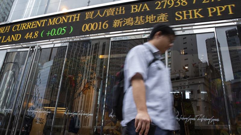 Seorang pejalan kaki berjalan melewati papan ticker elektronik yang menampilkan angka harga saham di luar kompleks Exchange Square di Hong Kong./ Justin Chin - Bloomberg