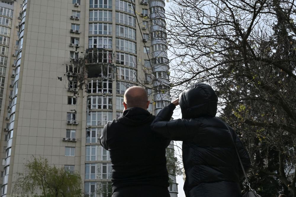 Orang-orang melihat bangunan perumahan bertingkat yang rusak akibat sisa-sisa drone Rusia yang ditembak jatuh di Kyiv pada 8 Mei./Bloomberg/Getty Images