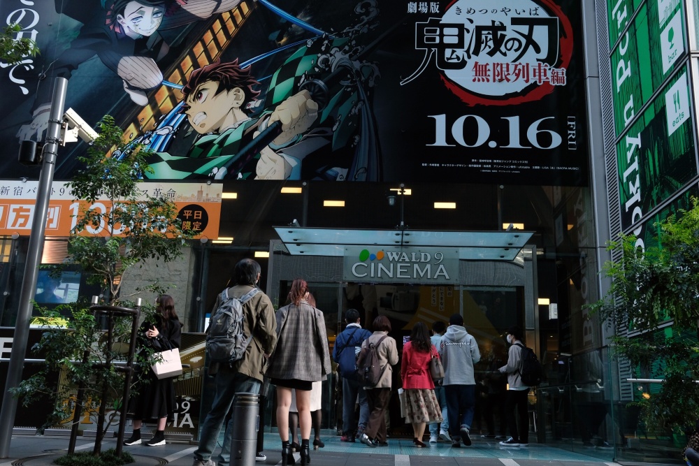 Penonton film berbaris di bawah iklan film Demon Slayer: Mugen Train di luar bioskop di Distrik Shinjuku Tokyo, Jepang, pada Sabtu, 31 Oktober 2020. Film ini telah memecahkan banyak rekor sejak dibuka sebelumnya, dan menjadi box office terbesar di Jepang. / Bloomberg-Takaaki Iwabu