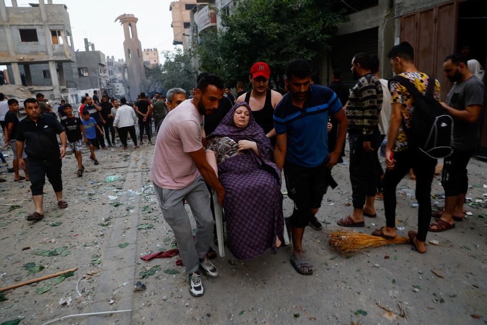 Warga Palestina membawa seorang wanita di jalan yang dipenuhi puing-puing pasca serangan Israel, menyusul serangan mendadak Hamas, di kamp pengungsi Beach, di Kota Gaza, 9 Oktober 2023. REUTERS/Mohammed Salem
