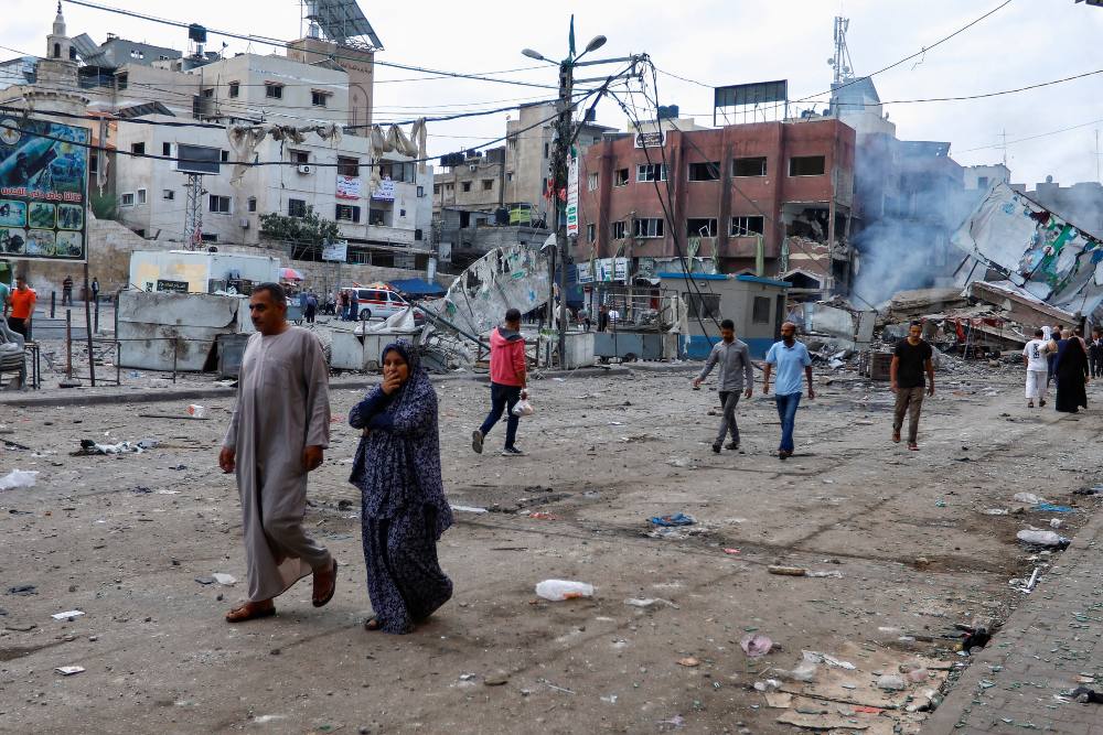 Warga Palestina berjalan di samping bangunan yang hancur akibat serangan Israel, di Khan Younis, Jalur Gaza selatan 10 Oktober 2023. REUTERS/Ibraheem Abu Mustafa