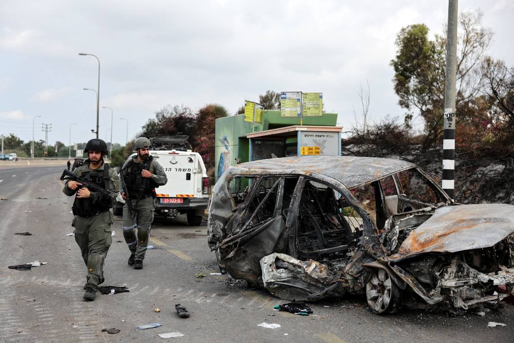 Polisi perbatasan Israel berjalan melewati mobil yang terbakar saat roket diluncurkan dari Jalur Gaza menuju Israel, di Ashkelon, Israel selatan 10 Oktober 2023. REUTERS/Violeta Santos Moura