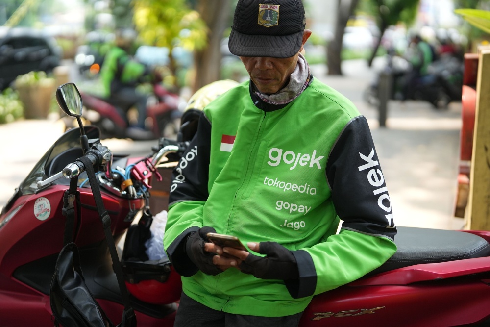 Seorang pengemudi Gojek melihat ponsel pintarnya di Jakarta, Indonesia, pada Senin (11/12/2023). Gojek merupakan salah satu layanan yang dikelola PT Goto Gojek Tokopedia Tbk (GOTO). - Bloomberg/Dimas Ardian