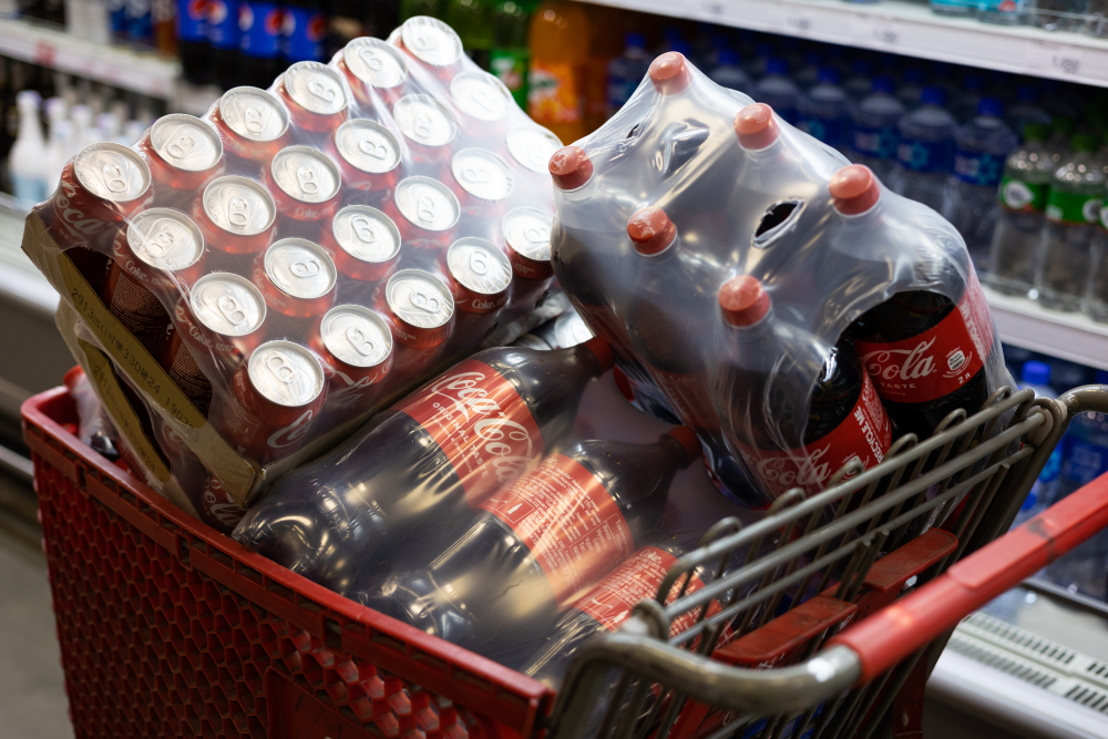 Kaleng dan botol minuman Coca-Cola dalam keranjang di salah satu supermarket. Kemenkeu menargetkan penerimaan negara dari implementasi cukai minuman manis senilai Rp3,8 triliun pada 2025. / Bloomberg-SeongJoon Cho