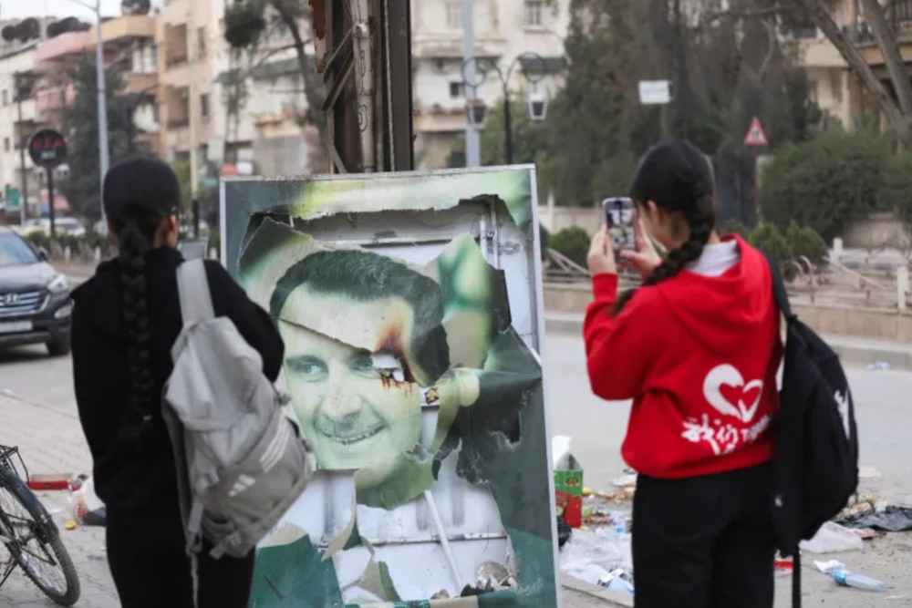 Warga Qamishli di Suriah menggunakan telepon genggam mereka untuk mengambil gambar Presiden Suriah Bashar al-Assad yang rusak ketika orang-orang merayakannya setelah pengumuman oleh pejuang oposisi bahwa mereka telah menggulingkan sang presiden. REUTERS/Orhan Qereman