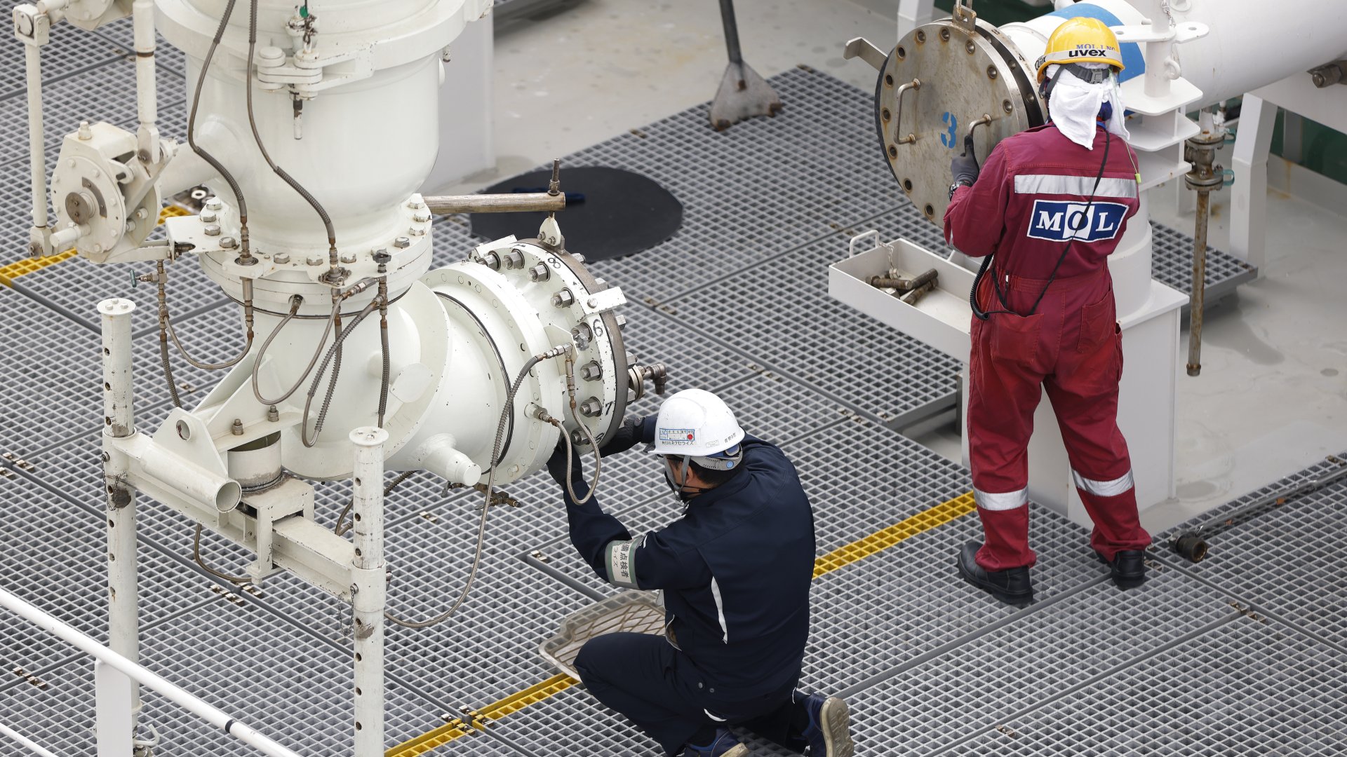 Pekerja bersiap menyambungkan pipa transfer gas alam cair (LNG), kiri, ke kapal tanker LNG Sohshu Maru, yang berlabuh di Stasiun Tenaga Listrik Termal Futtsu milik Jera Co. di Futtsu, Prefektur Chiba, Jepang, Jumat (17/12/2021). Bloomberg/Kiyoshi Ota.