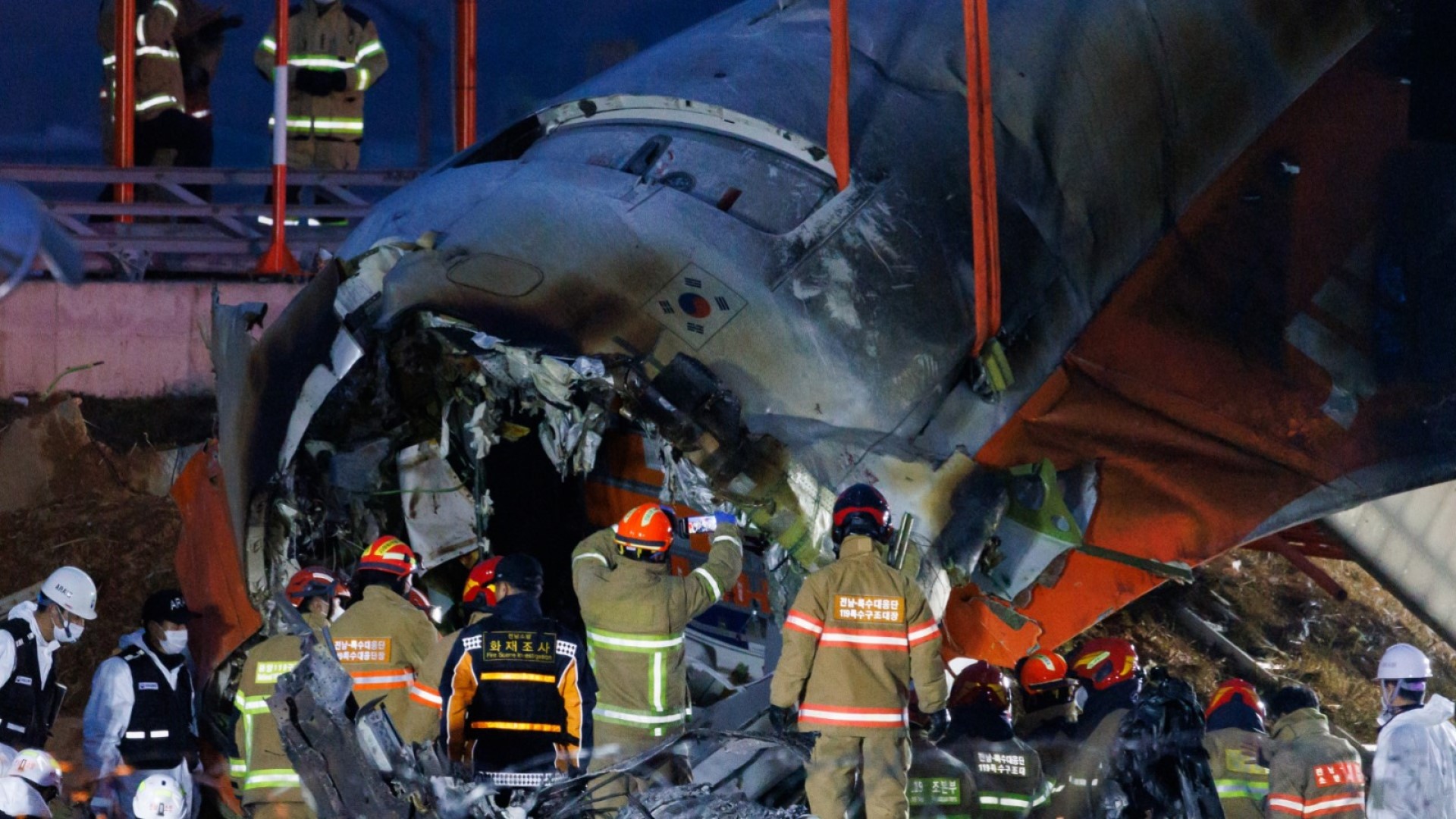 Anggota tim penyelamaberada di depan reruntuhan pesawat Jeju Air Co. Penerbangan 2216 di Bandara Internasional Muan, Korea Selatan, pada Minggu, 29 Desember 2024. Pesawat Boeing Co. 737-800 yang dioperasikan oleh Jeju Air jatuh terbakar di landasan pacu, mengakibatkan 179 orang meninggal./ Bloomberg-SeongJoon Cho.