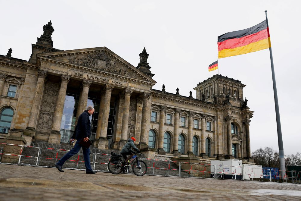 Pengendara sepeda dan pejalan kaki melewati gedung Reichstag saat bendera nasional Jerman berkibar, pada hari pemungutan suara kepercayaan yang diserukan oleh Kanselir Jerman Olaf Scholz, 16 Desember 2024./REUTERS