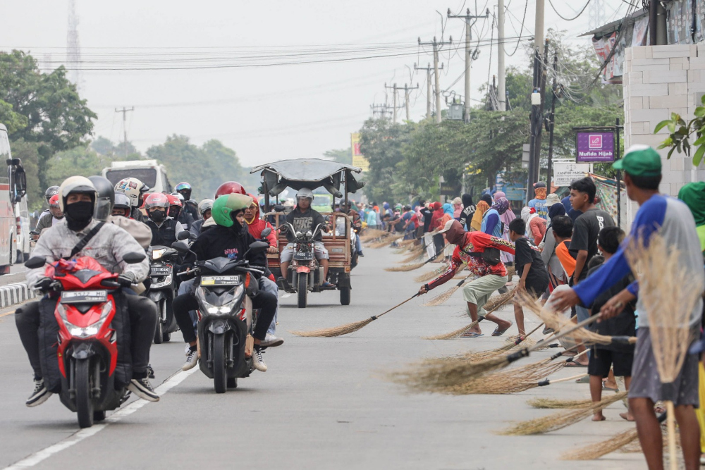 Sejumlah warga mengais uang sedekah yang dilempar pengendara saat melintas di Jembatan Sewo, Kabupaten Subang, Jawa Barat, Senin (8/4/2024). Aksi mengambil uang sedekah menggunakan sapu tersebut dapat membahayakan keselamatan pengguna jalan terutama saat arus mudik. - Bisnis/Eusebio Chrysnamurti