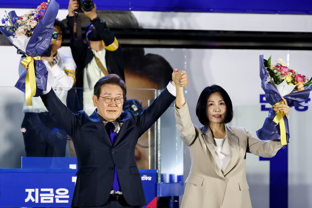 Calon Presiden Korea Selatan dari Partai Demokrat Lee Jae-Myung (kiri) dan istrinya Kim Hye-gyeong (kanan) di acara malam pemilihan umum di Seoul, Korea Selatan pada Rabu (4/6/2025). Lee diproyeksikan akan memperoleh 51,7% suara, menurut jajak pendapat gabungan oleh tiga lembaga penyiaran Korea Selatan, KBS, MBC, SBS. / Bloomberg-SeongJoon Cho